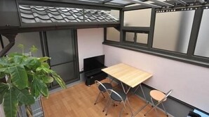 A small room with a wooden table and four chairs, a large potted plant, and a television. - BJ Family Inn (Kyoto)