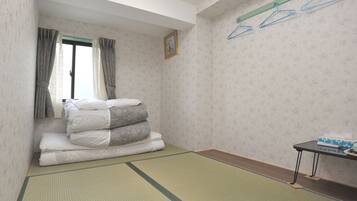 A room with tatami flooring, a bed with pillows, a window with curtains, a wall-mounted hanger, and a small table with a tissue box.