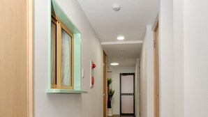 A hallway with wooden flooring, a window with a green frame, and a door at the end. - BJ Family Inn (Kyoto)