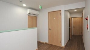 A hallway with wooden flooring, white walls, and a green safety sign. - BJ Family Inn (Kyoto)