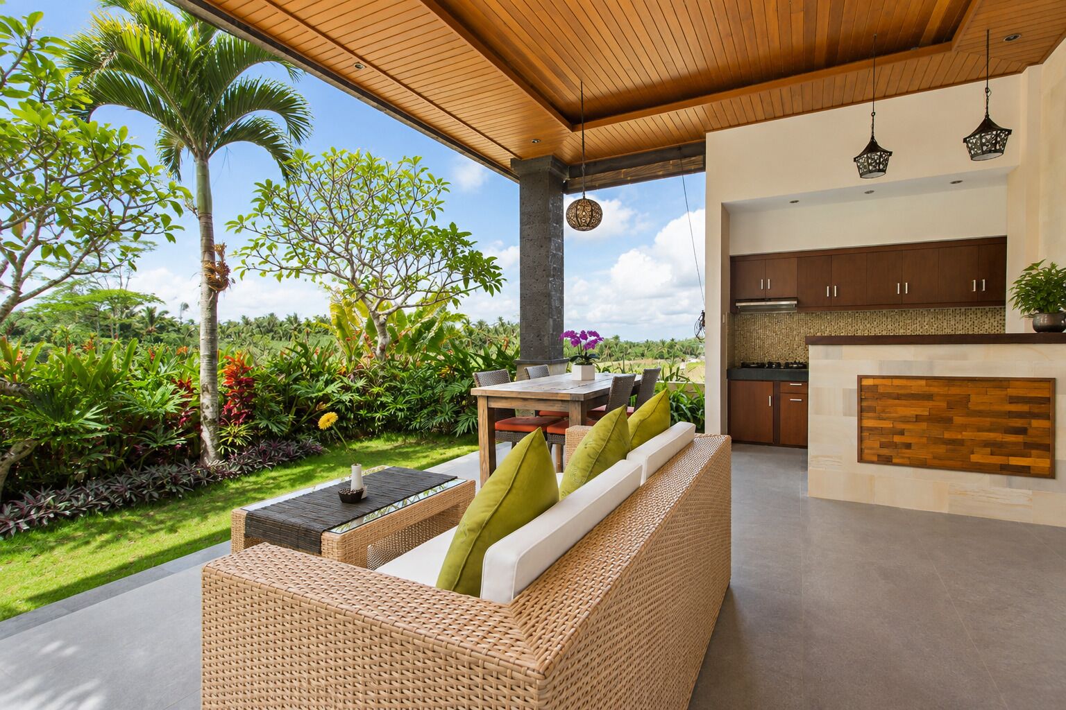 Un espacio exterior moderno con una zona de estar con sofá de mimbre, una mesa de comedor y una cocina con armarios de madera.