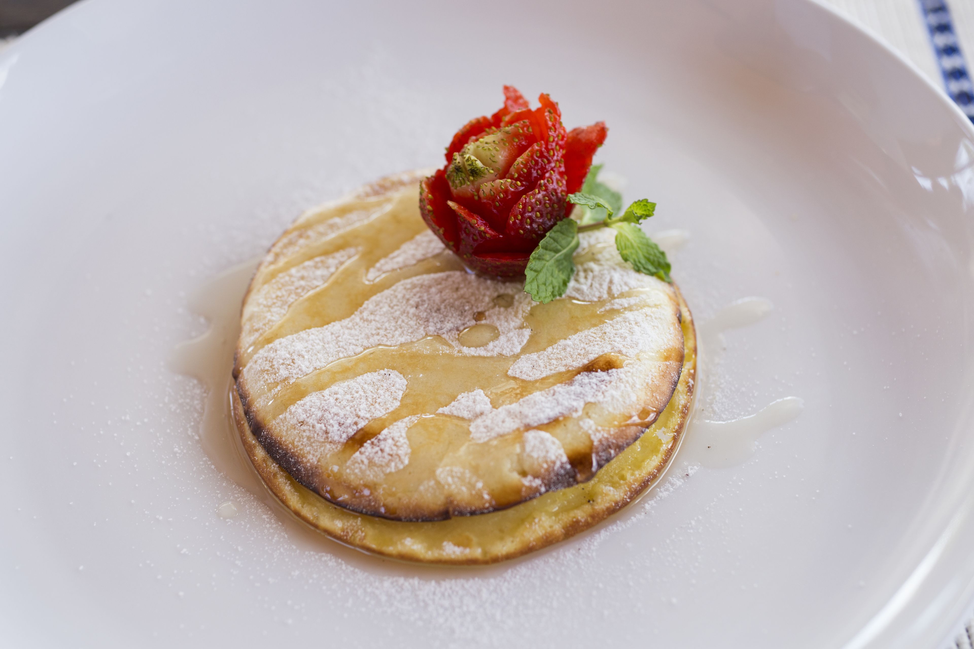 A dessert on a white plate with powdered sugar and a strawberry on top.