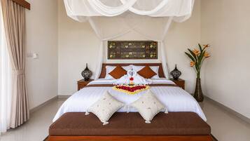 A neatly made bed with a canopy, a bedside table with a lamp, and a vase with flowers.
