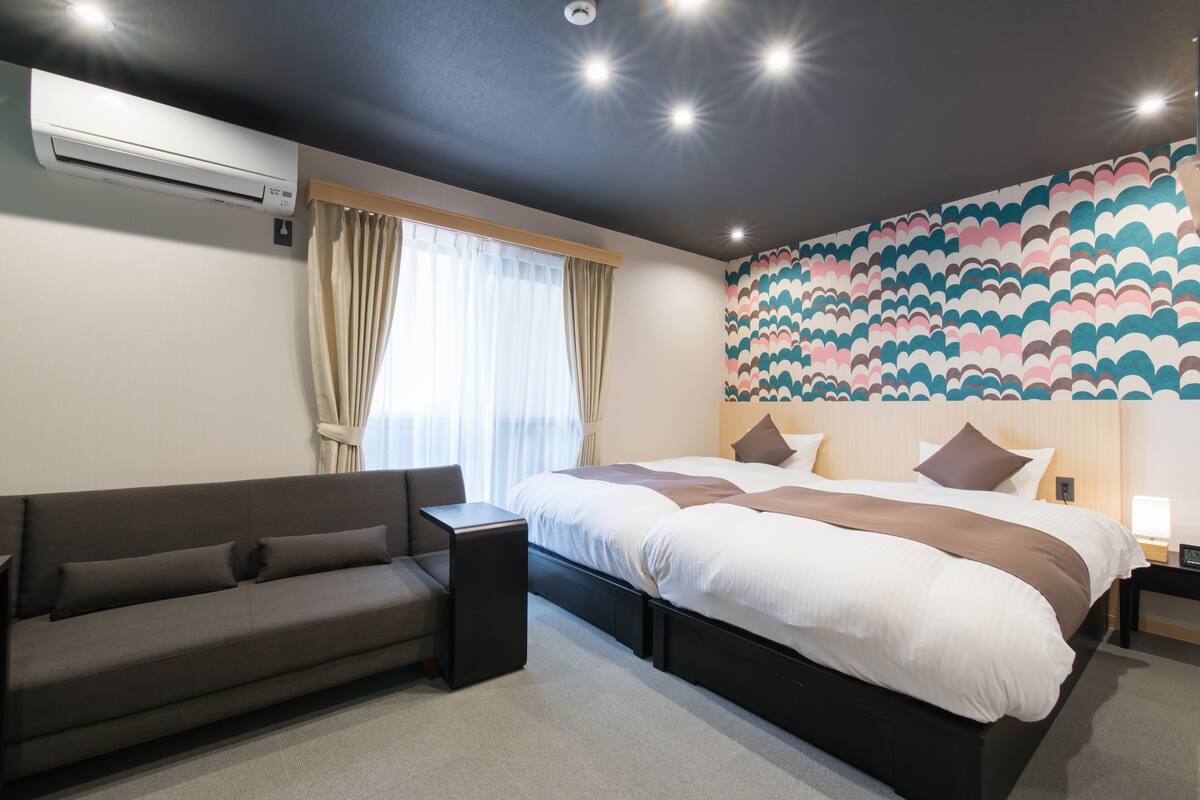 Una habitación de hotel moderna con una cama grande, un sofá, un equipo de aire acondicionado y una pared con diseño.
