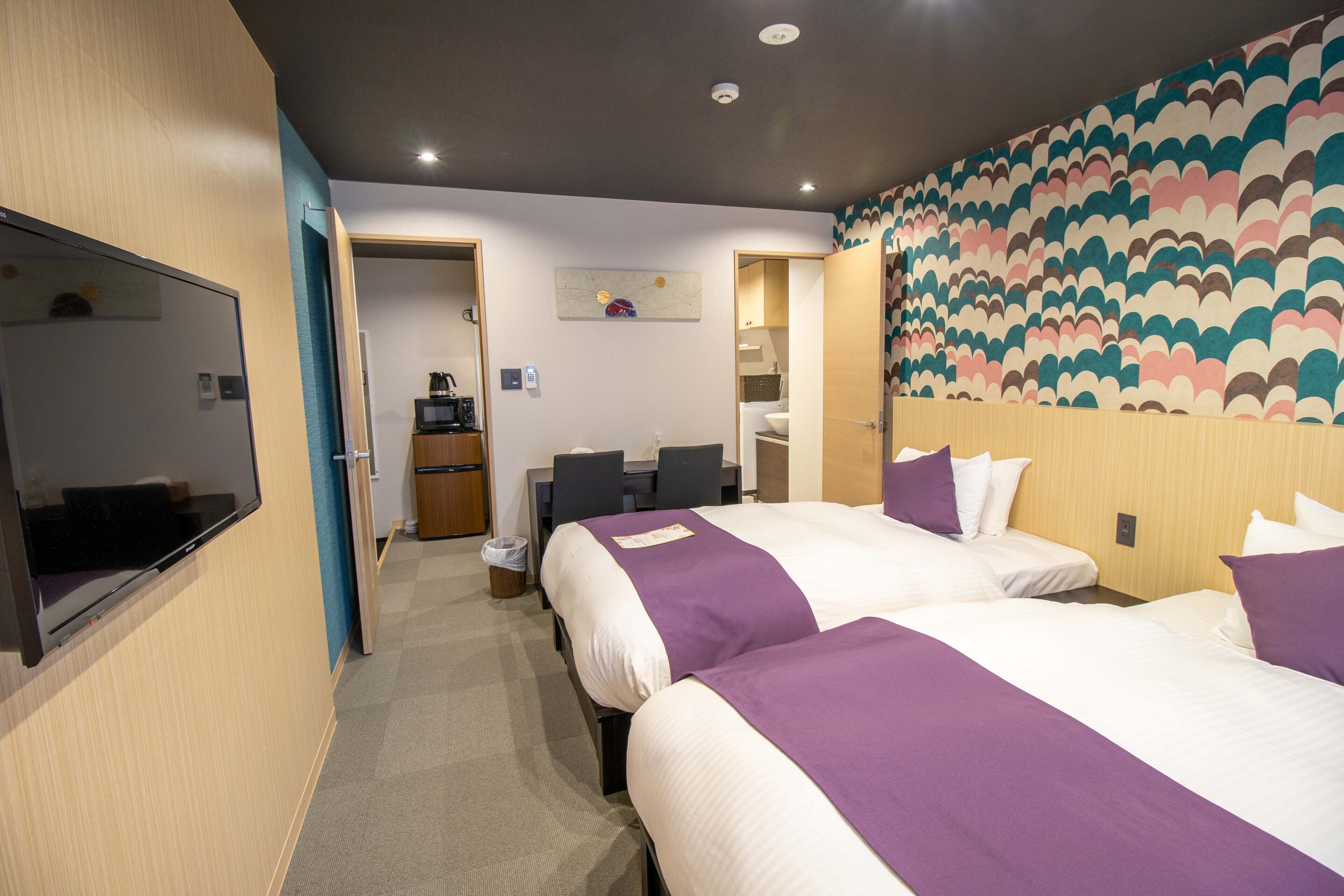 A hotel room with two beds, a TV, a desk, and a bathroom.