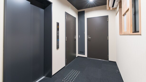 Un couloir avec trois portes d’ascenseur, un panneau de commande et une étagère en bois sur laquelle sont posés divers objets.