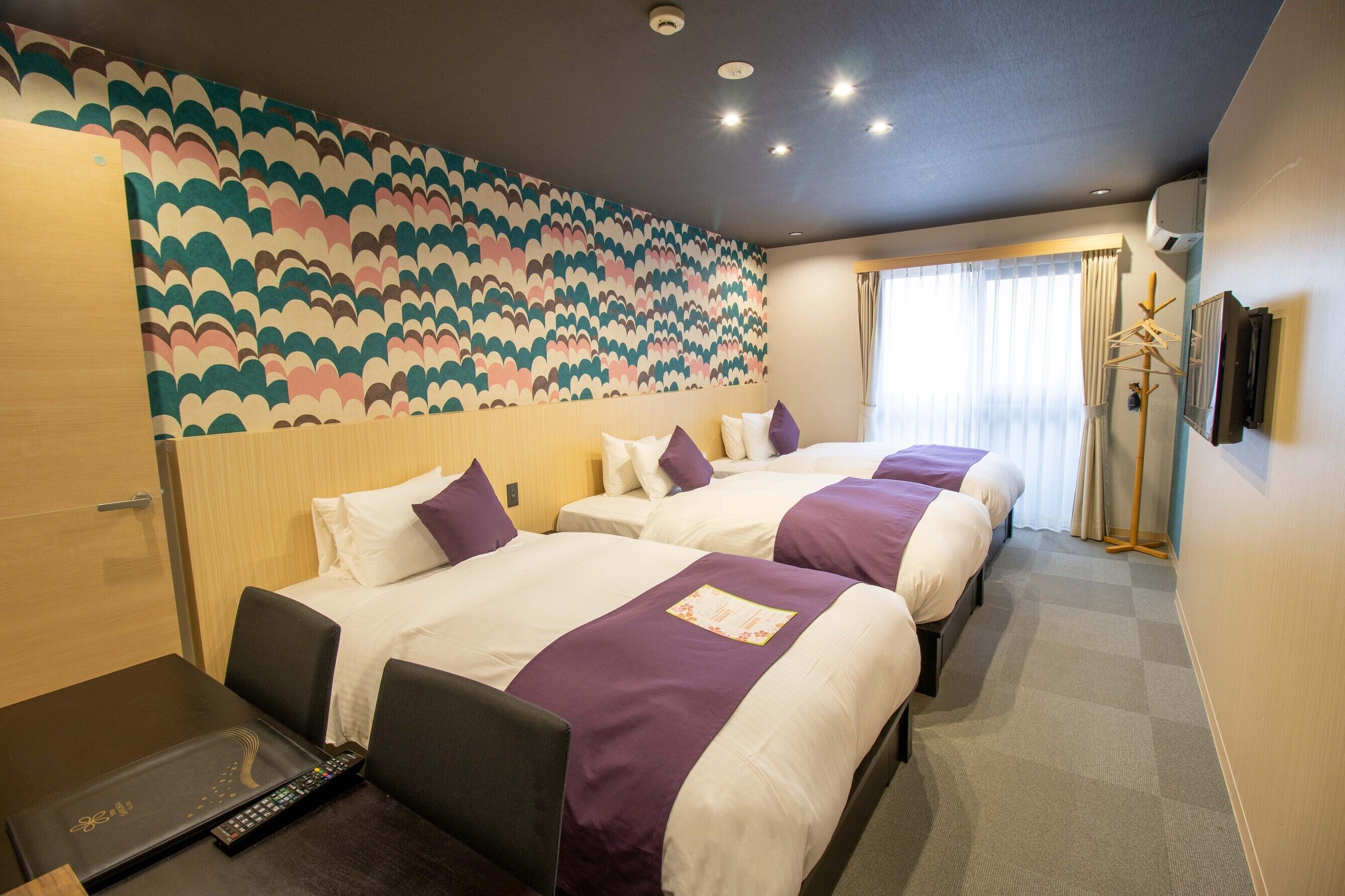 Une chambre d’hôtel avec deux lits, un bureau avec un ordinateur portable, une télécommande et un mur décoré d’un motif.