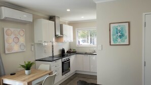 A modern kitchen with white cabinets, a black countertop, and a built-in oven. There is a dining table with chairs and a potted plant.