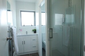 A modern bathroom with a glass shower enclosure, a window above the sink, and a potted plant on the countertop. - Rose Apartments and Spa (Rotorua)