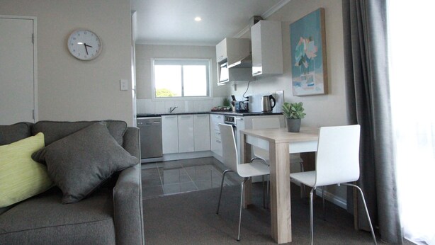 A modern kitchen with white cabinets, a dining area with a wooden table and white chairs, and a gray sofa with cushions.