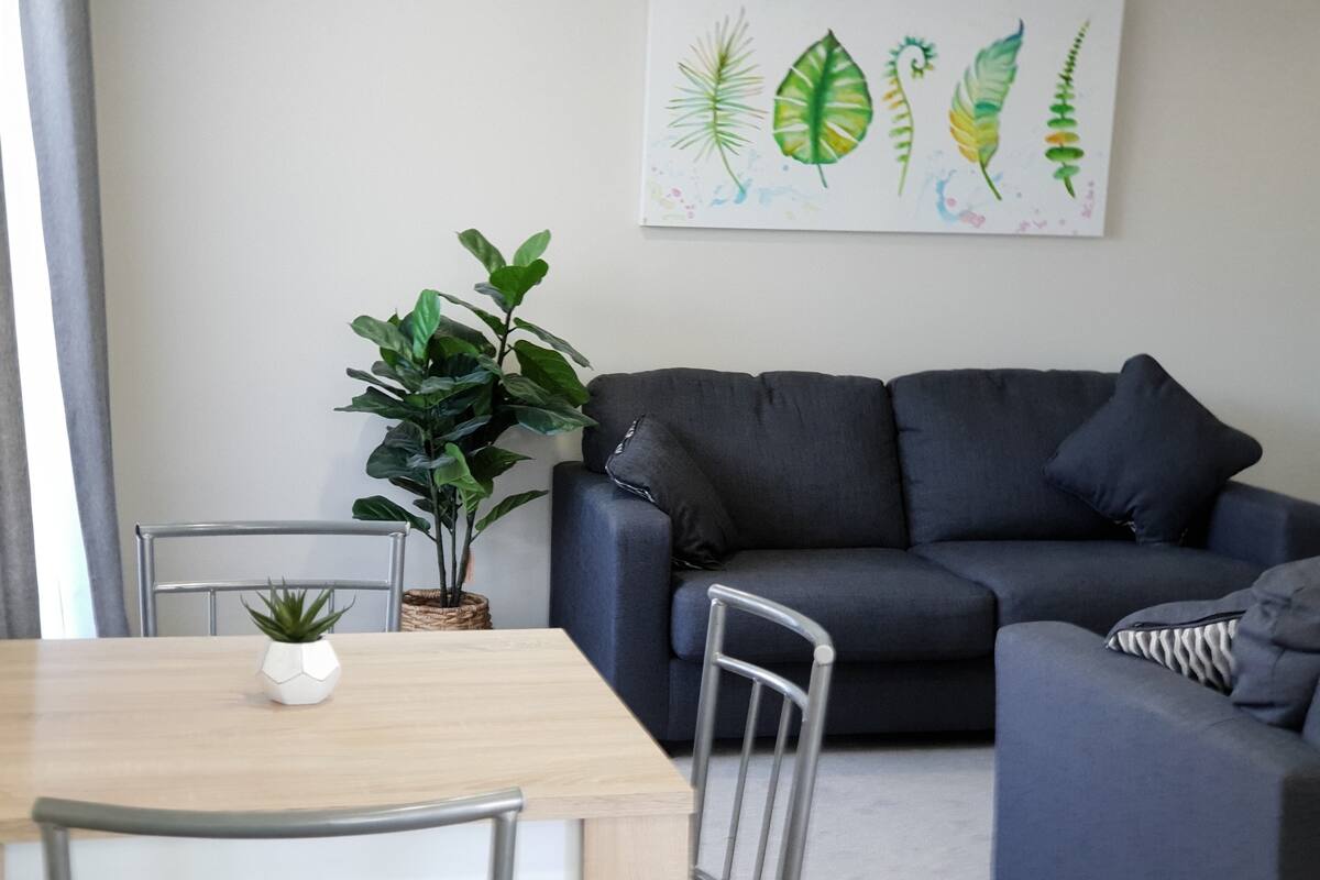 A modern living room with a grey sofa, a wooden dining table, and a potted plant.