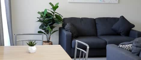 Een moderne woonkamer met een grijze bank, een houten eettafel en een plant in een pot.