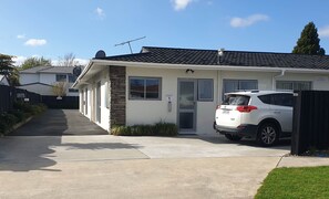 A single-story house with a white exterior, a stone accent wall, and a garage door. - Rose Apartments and Spa (Rotorua)