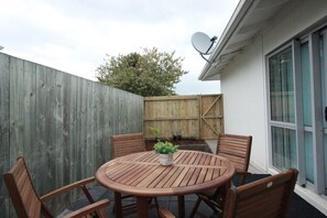 A wooden table and chairs in a backyard with a wooden fence and a satellite dish. - Rose Apartments and Spa (Rotorua)