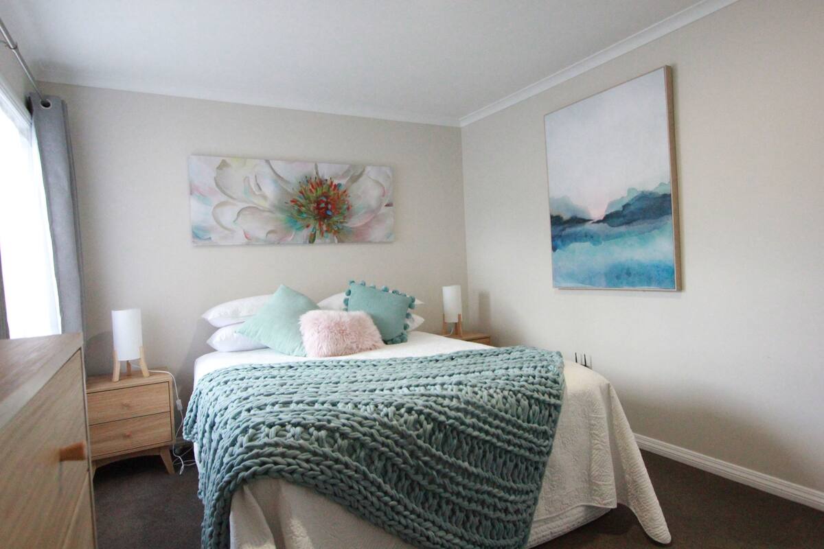 A bedroom with a bed, nightstands, a dresser, and two wall-mounted paintings.