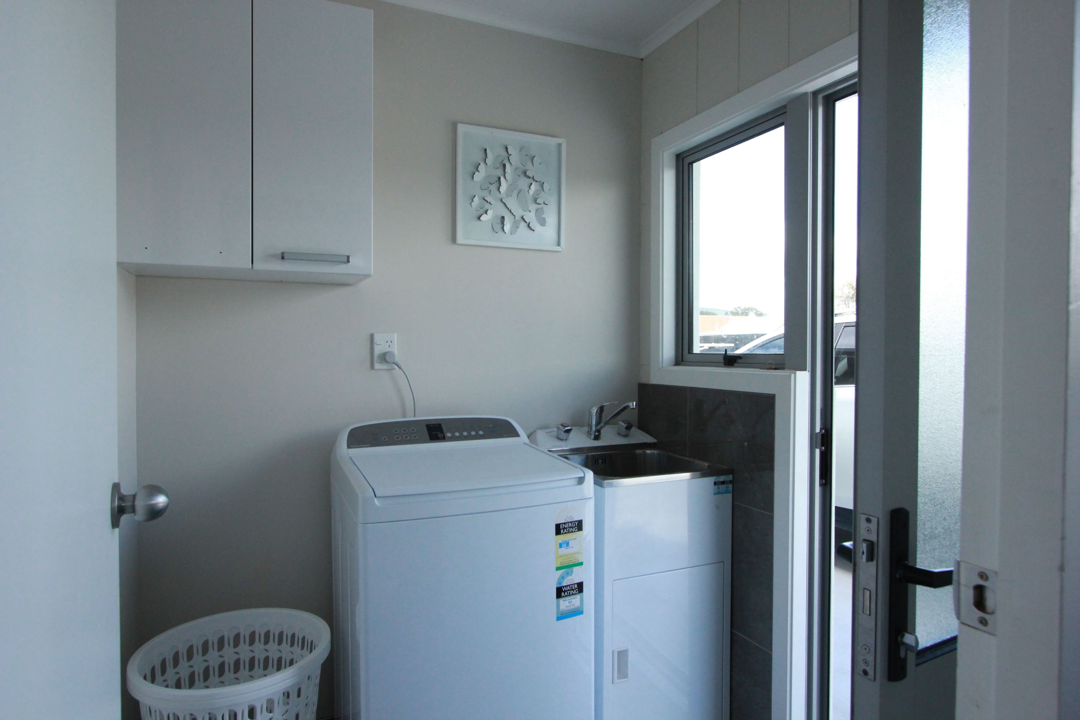 A laundry area with two white washing machines, a small sink, and a window.