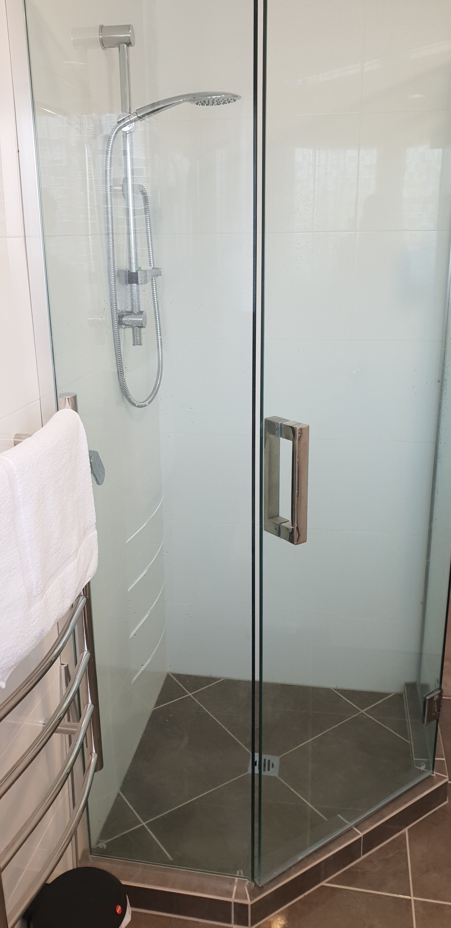 A glass-enclosed shower with a handheld showerhead and a wall-mounted faucet.