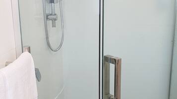 A glass-enclosed shower with a handheld showerhead and a wall-mounted faucet.