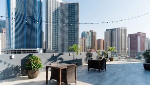 Una terraza en la azotea con mobiliario exterior y plantas en macetas, con vistas a un paisaje urbano de edificios altos.