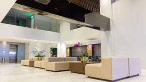 Un lobby moderno con techo alto, suelo de mármol y una zona de estar con sofás y una planta.