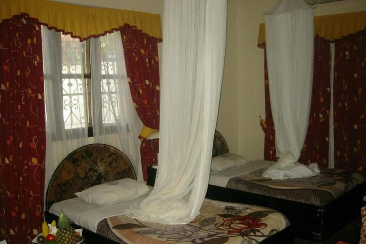 A room with two beds, each with a canopy. There are curtains on the windows, and a bed on the left has a fruit bowl on it.