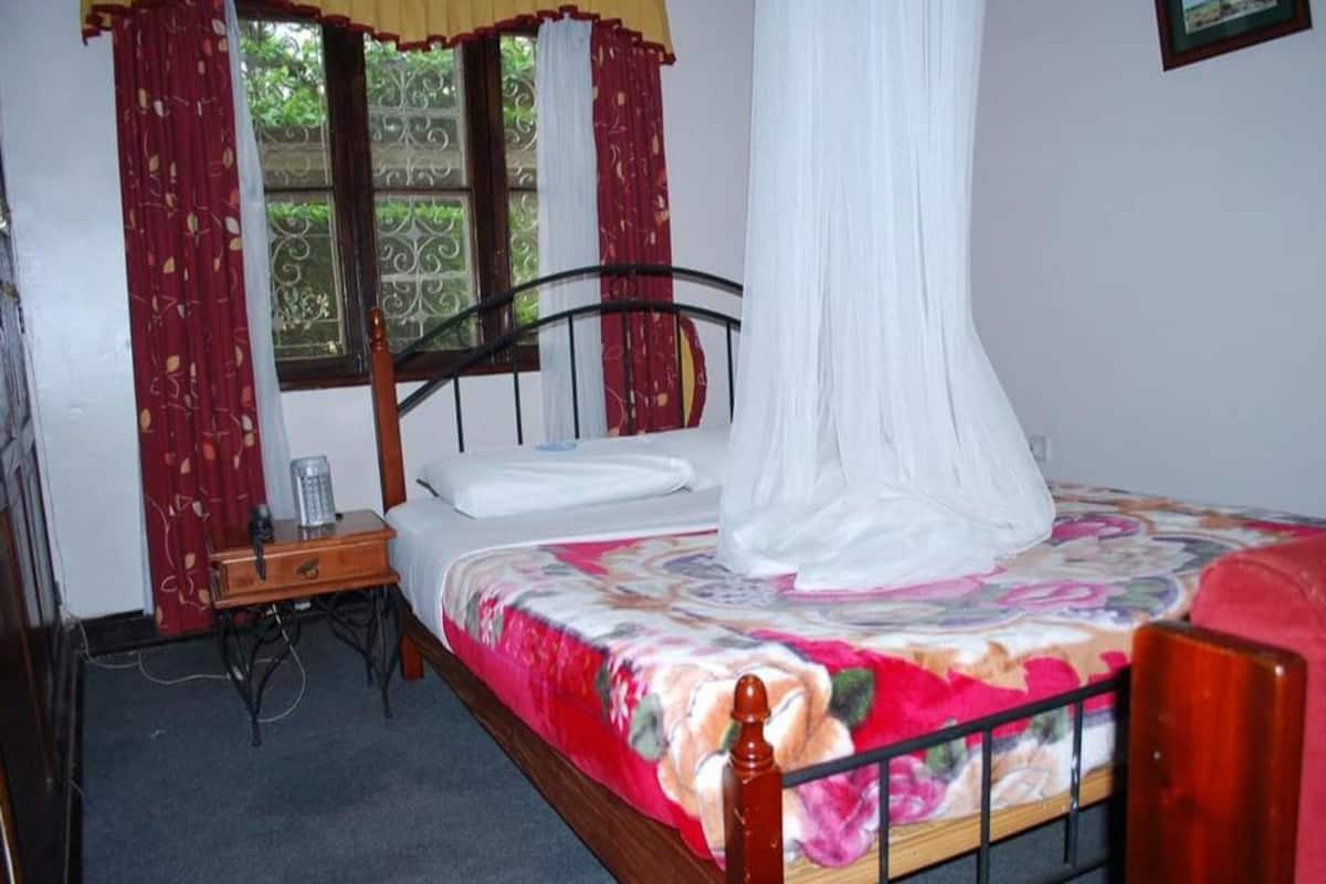 A bedroom with a bed, a bedside table, a lamp, and curtains.