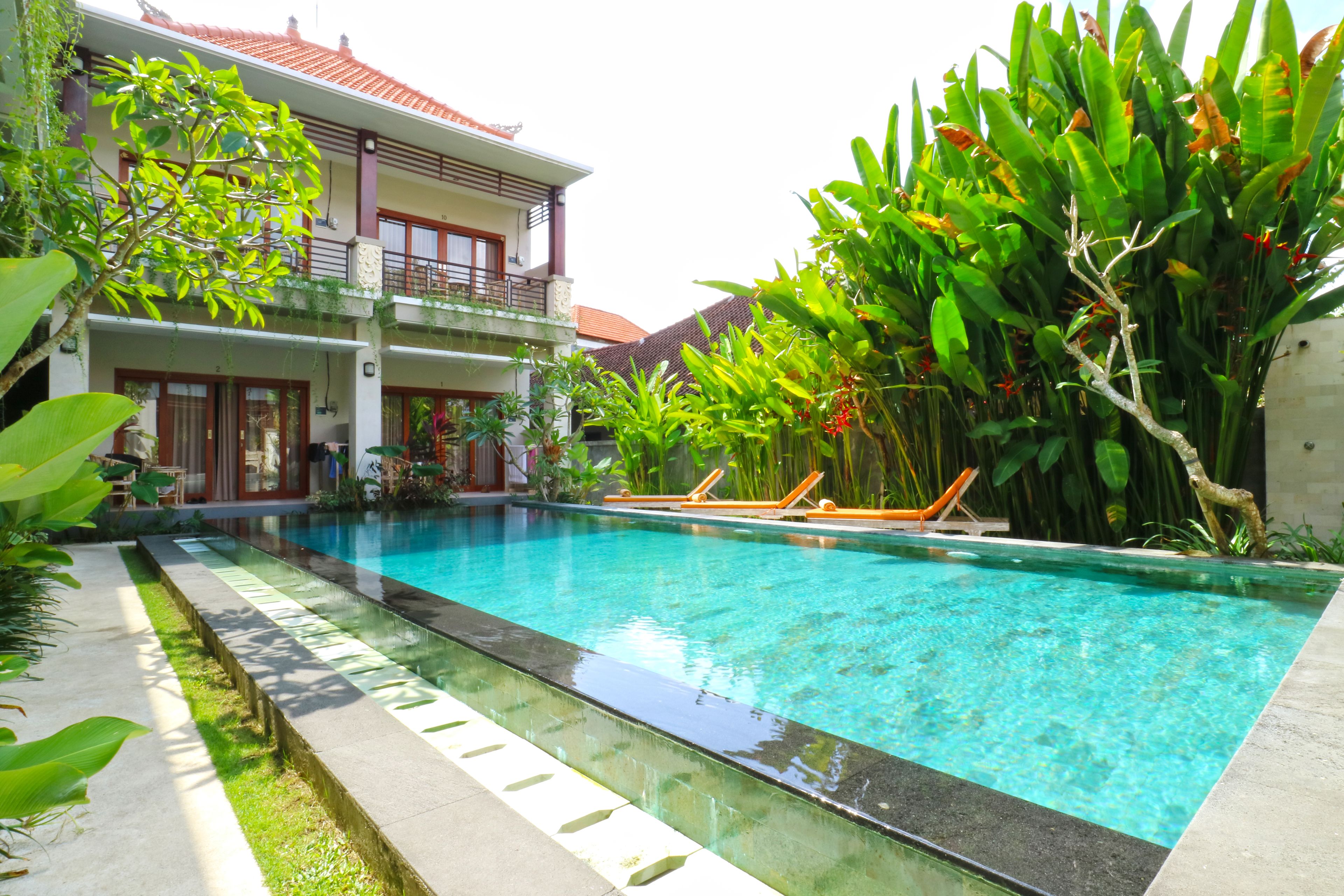 A swimming pool with lounge chairs, surrounded by lush greenery and a two-story building with balconies.