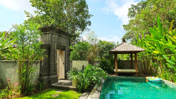 Una piscina rodeada de exuberante vegetación, una estructura de piedra y un pabellón.