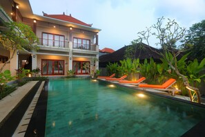 Un bâtiment à deux étages doté d’une piscine, de chaises longues et de plantes tropicales.