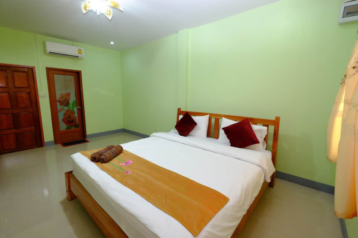 A hotel room with a bed, a wooden headboard, a brown throw blanket, and a floral painting on the door.