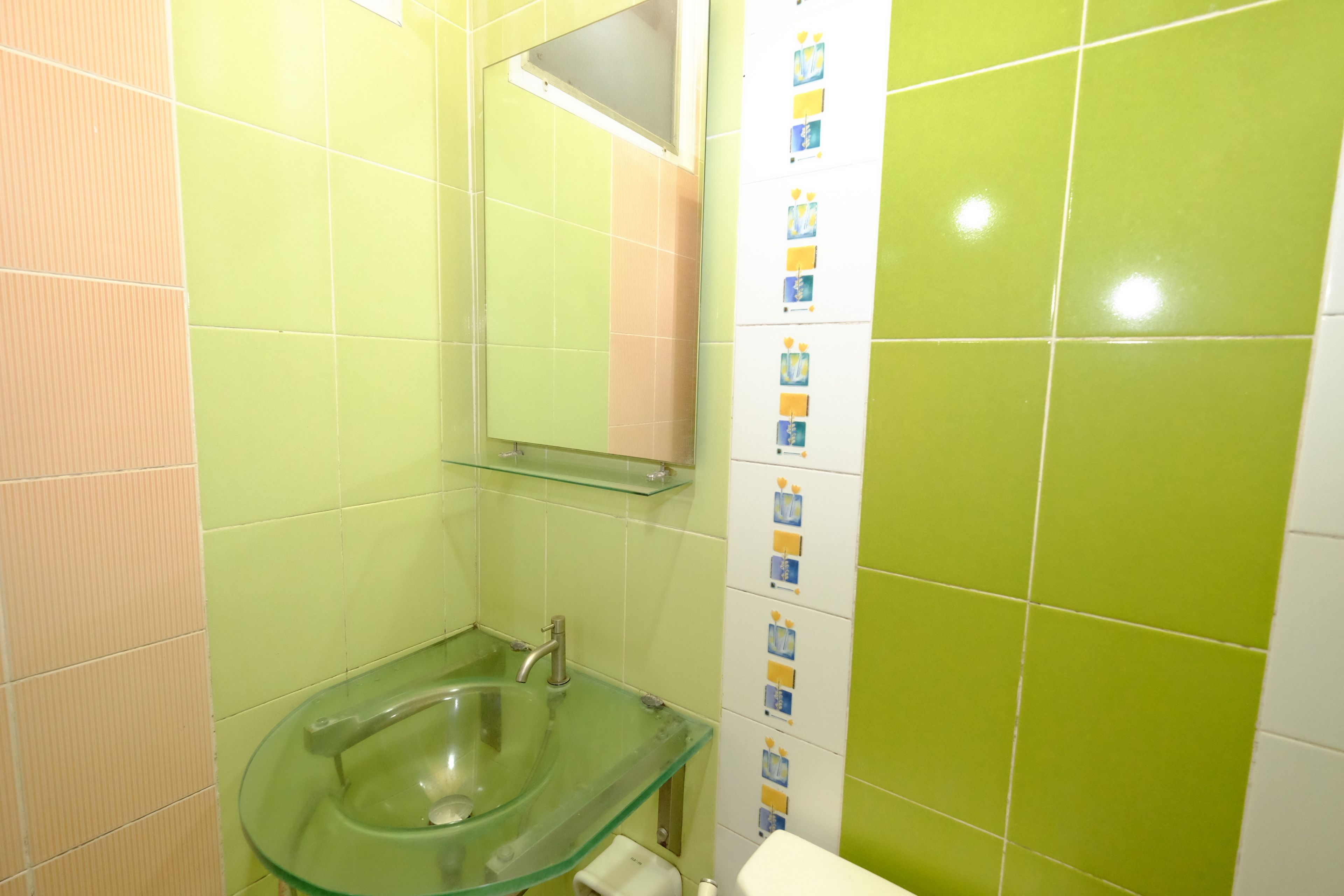 A bathroom with a glass sink, a mirror, and green and white tiles.