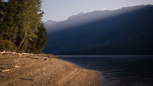A lakeside view with mountains in the background and a rocky shoreline. - Rustic luxury in the wilderness, by the beach with lake views (Central Kootenay D)