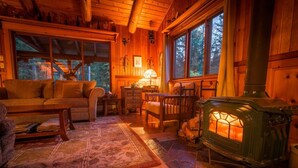 A cozy cabin interior with a wooden interior, a fireplace, a sofa, a dining table, and a rug. - Rustic luxury in the wilderness, by the beach with lake views (Central Kootenay D)
