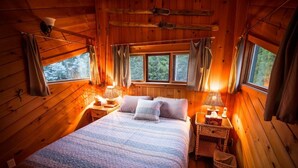 A cozy wooden cabin bedroom with a bed, two bedside tables, and a window with curtains. - Rustic luxury in the wilderness, by the beach with lake views (Central Kootenay D)