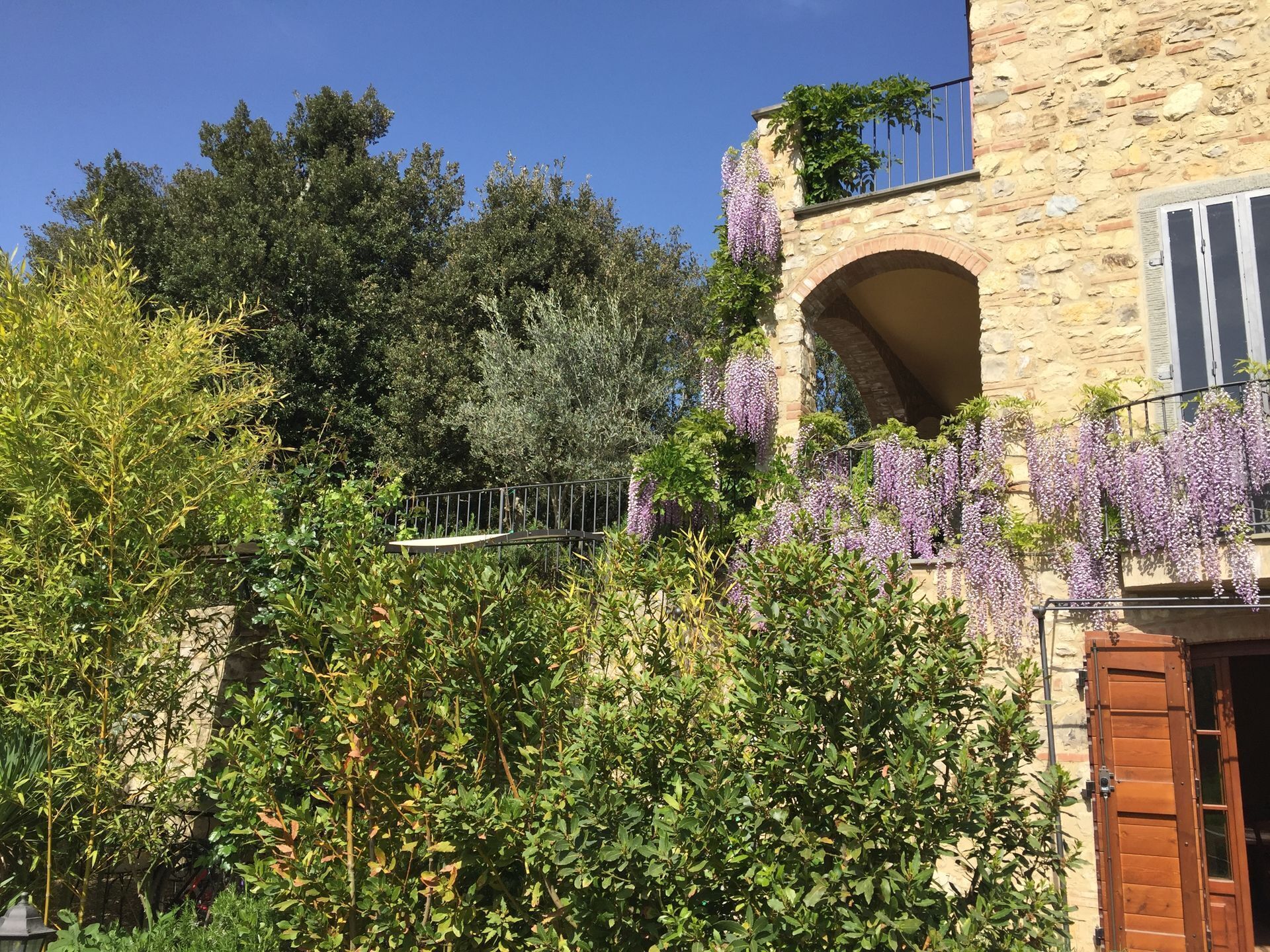 A stone building with a wooden door and a balcony with purple flowers.