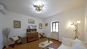A living room with a white sofa, a wooden cabinet, a television, and a window with curtains. - Podere Le Volte - Country House (Pergine Valdarno)