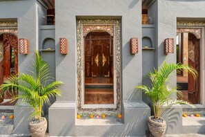 Fachada de edificio con puertas de madera ornamentadas, plantas en macetas y paneles decorativos en la pared.