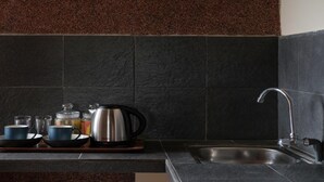A kitchen with dark tiles, a stainless steel kettle, and a sink. - Grand Ashanti Villa (Ubud)