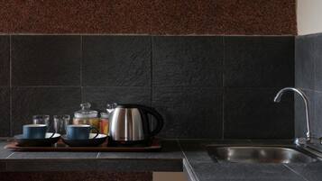 Una cocina con baldosas oscuras, un hervidor de acero inoxidable y un lavabo.