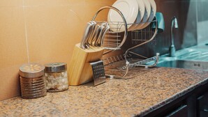 A kitchen counter with a dish rack holding plates, a wooden utensil holder, and two salt shakers. - Grand Ashanti Villa (Ubud)