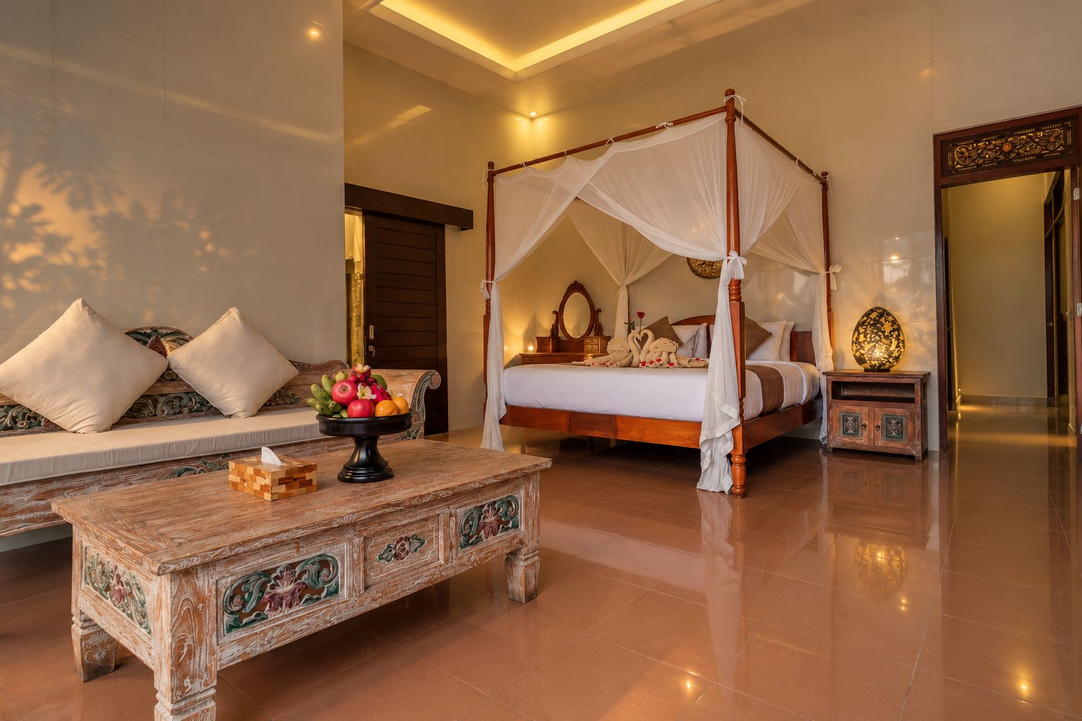 A four-poster bed with a canopy, a sofa with cushions, a wooden coffee table with fruit, and a decorative mirror.