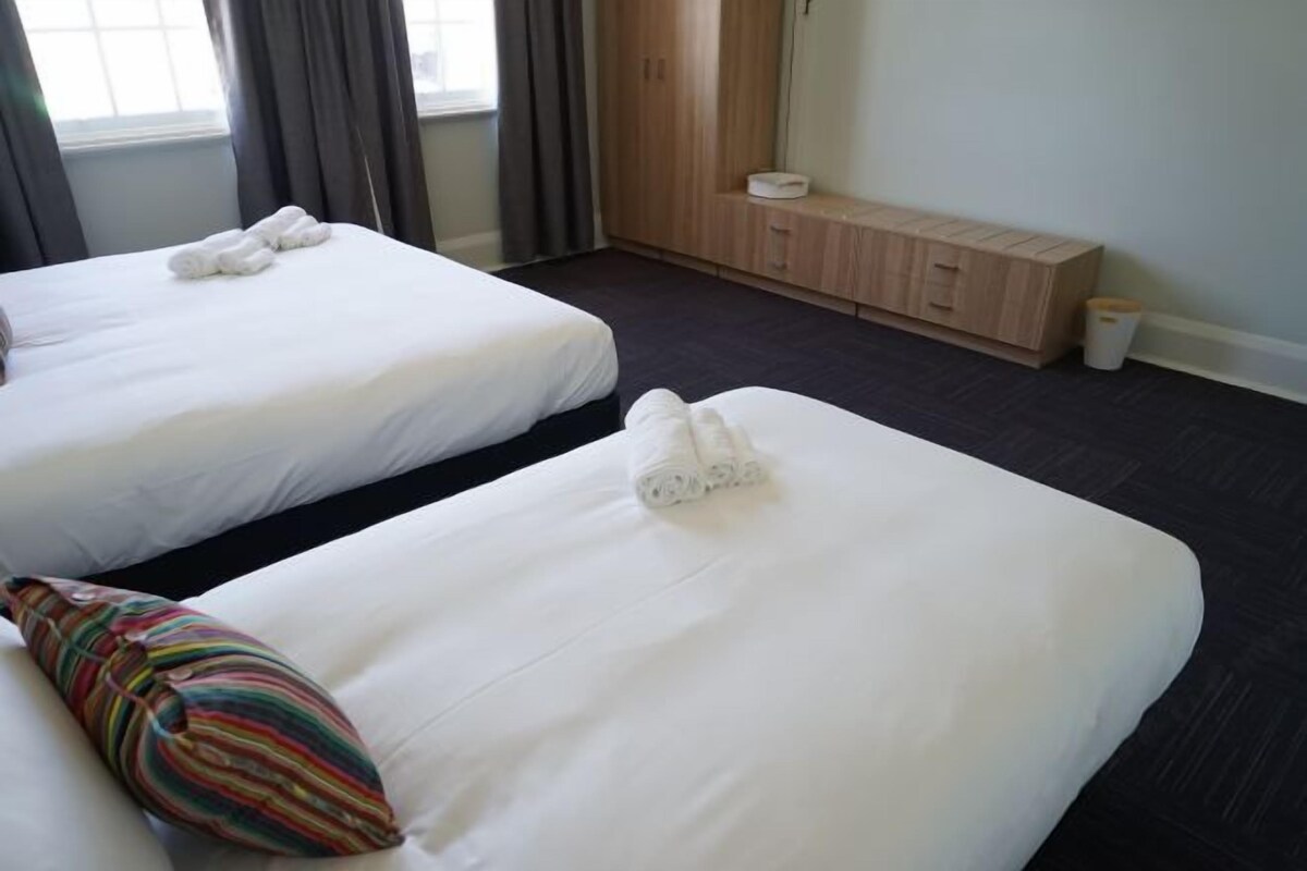 Two single beds with white linens and towels, a colorful striped pillow, a wooden cabinet, and a small trash bin.