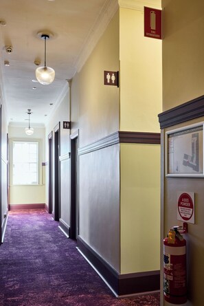 Un pasillo de hotel con extintor, plano de evacuación y señalización de baños de hombres y mujeres.
