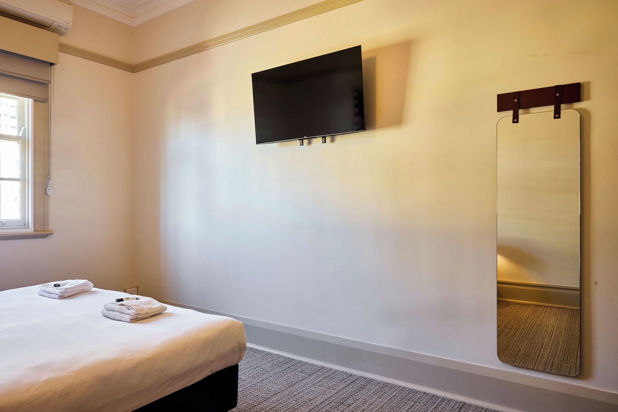 A hotel room with a bed, a flat-screen TV mounted on the wall, and a large mirror.