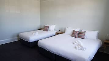 A hotel room with two beds, each with white bedding and pillows, and a dark wood floor.