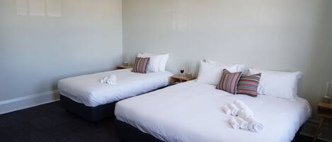 Habitación de hotel con dos camas, cada una con ropa de cama y almohadas blancas, y suelo de madera oscura.