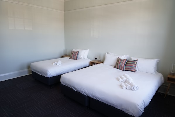 Habitación de hotel con dos camas, cada una con ropa de cama y almohadas blancas, y suelo de madera oscura.