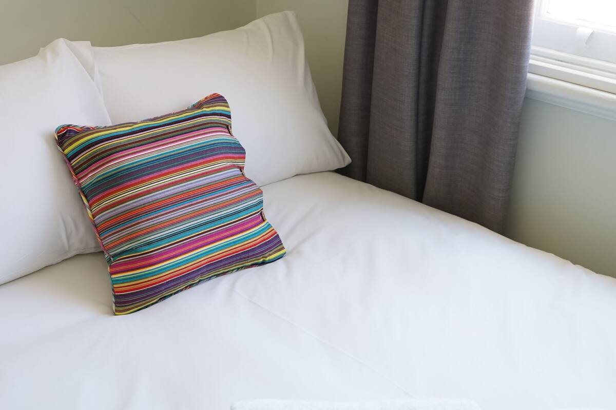 A neatly made bed with white linens, a colorful striped pillow, and rolled white towels.