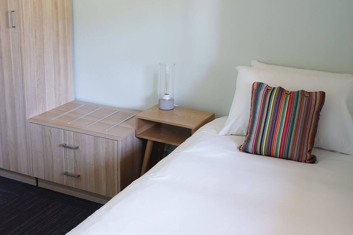 A hotel room with a bed, a wooden wardrobe, a nightstand, and a lamp.
