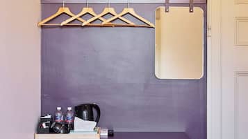 A small room with a purple wall, a wooden bench with a mirror, a coat rack, a trash bin, and a door.